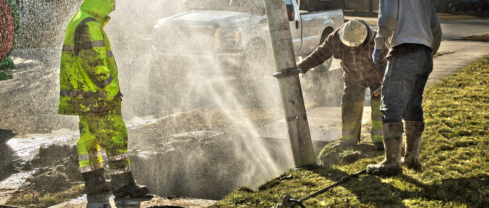 Muddy utility worker men fixing broken water line with droplets spraying into the air