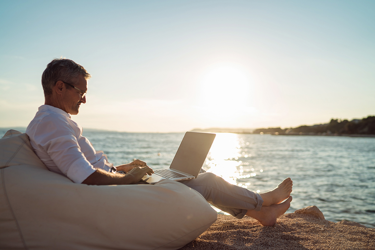 Businessman on beach reading laptop